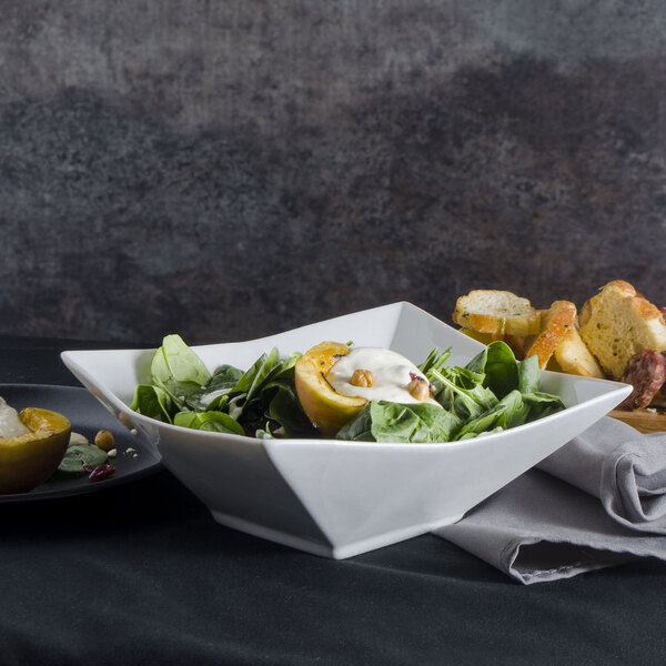 A 10 Strawberry Street Whittier Elite white porcelain bowl filled with salad next to a plate of bread.