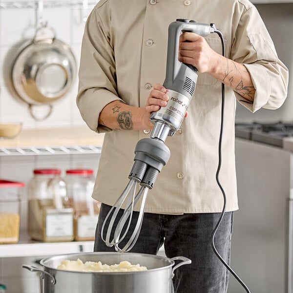 A Robot Coupe CMP250 Combi Compact 10-inch immersion blender with an 8-inch whisk attachment being used in a kitchen.