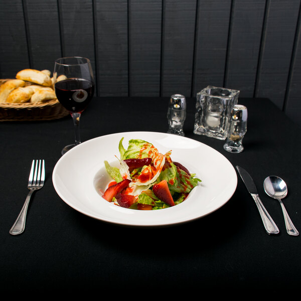 A plate of food with a Tao bowl of salad with strawberries and sauce on a black table.