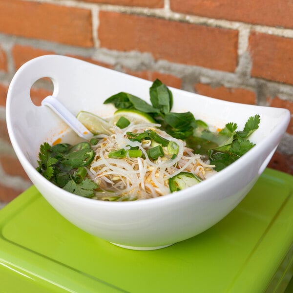A white porcelain bowl with cut outs holding a bowl of soup with noodles and vegetables.