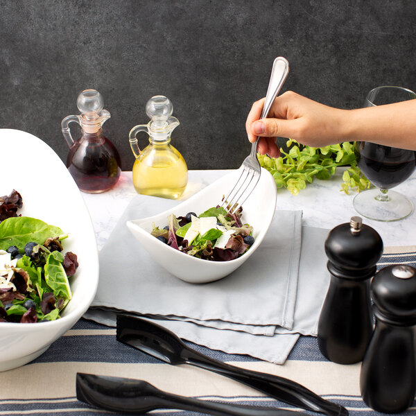 A hand holding a fork in a white porcelain cradle bowl filled with salad.