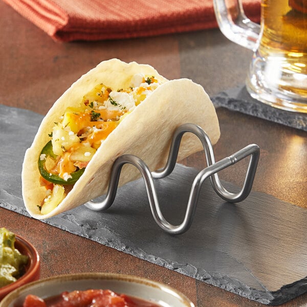 A Tablecraft Taco Taxi stainless steel taco holder with a taco on a stand on a table in a Mexican restaurant.
