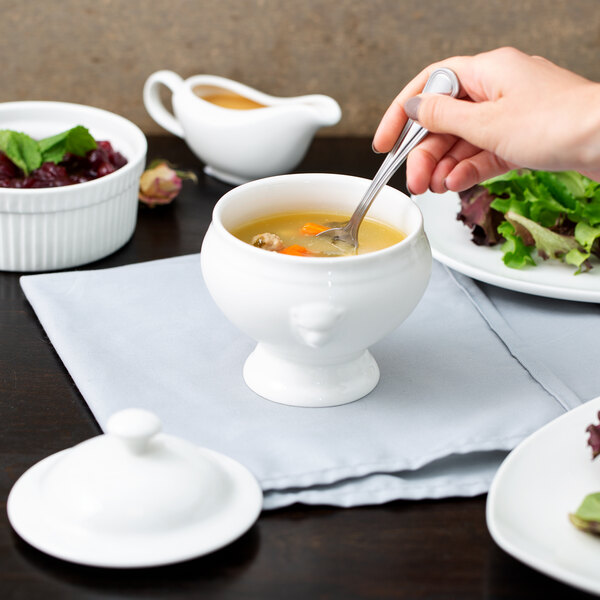 A person holding a spoon in a bowl of soup.