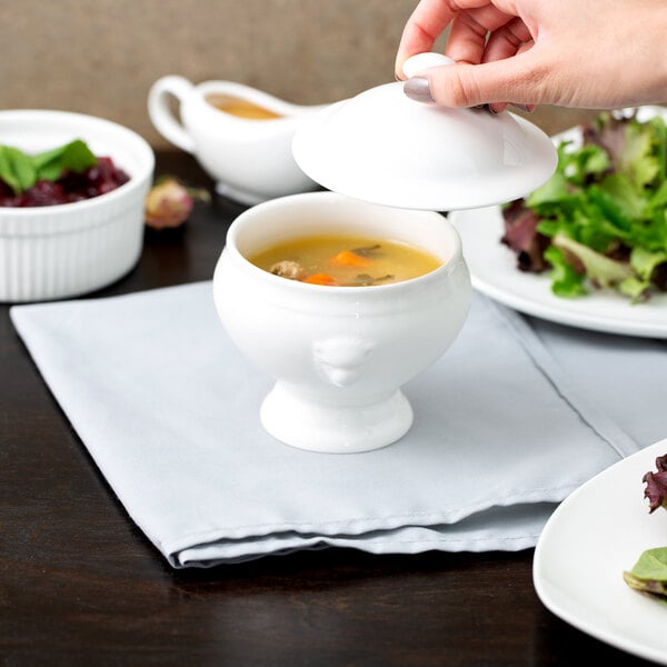 A person pouring soup into a white 10 Strawberry Street small lion head tureen.