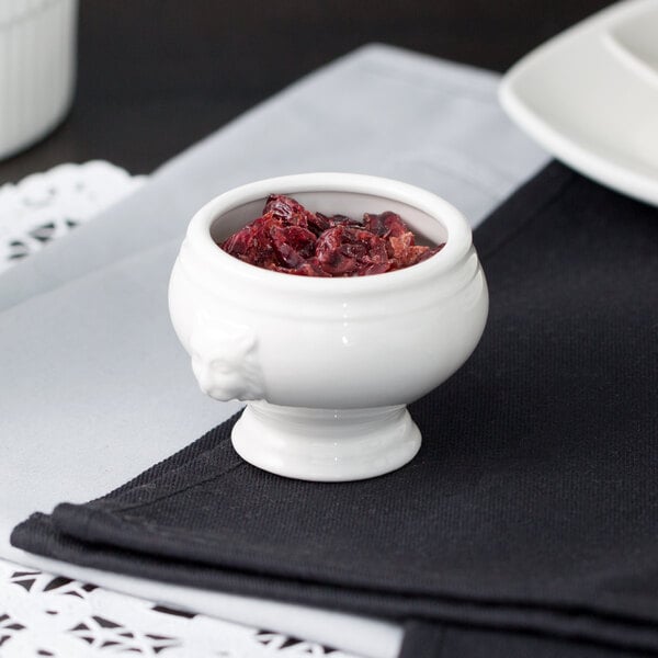 A white porcelain mini lion headed tureen filled with food on a table.