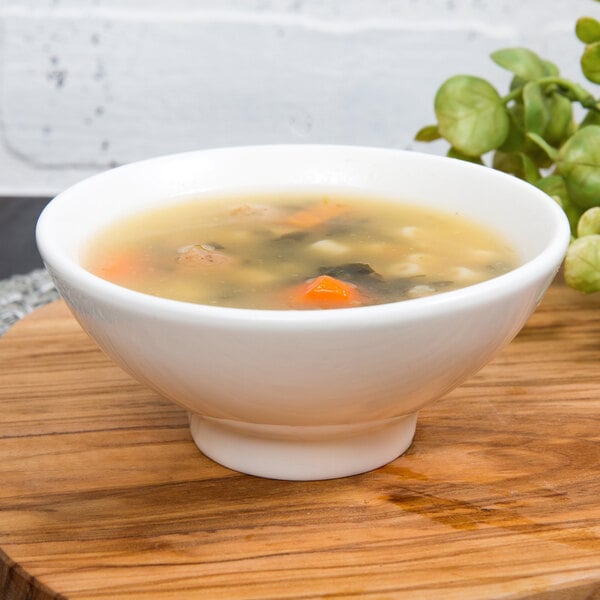 A 10 Strawberry Street Whittier white porcelain footed rice bowl filled with soup on a table.