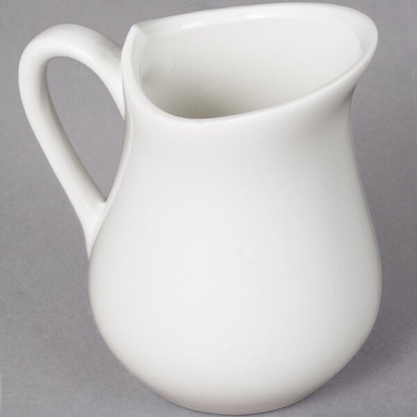 A white pitcher with a handle on a gray surface.