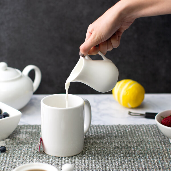 A person pouring milk into a white pitcher.