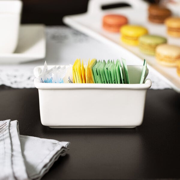 A white porcelain sugar packet holder with packets inside on a white surface.