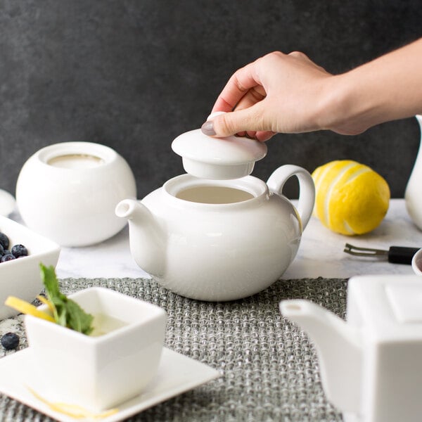 A person pouring tea into a white 10 Strawberry Street Whittier teapot.