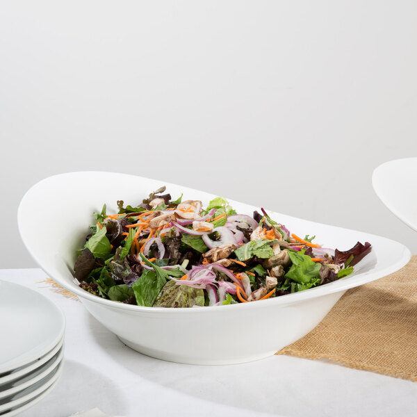 A white porcelain bowl filled with salad on a table with a stack of white plates.