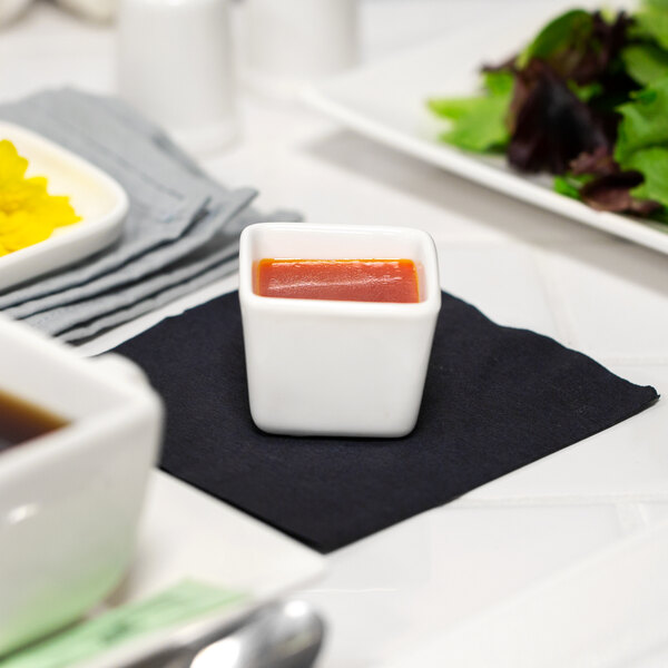 A white square 10 Strawberry Street porcelain bowl with red sauce on a black napkin.