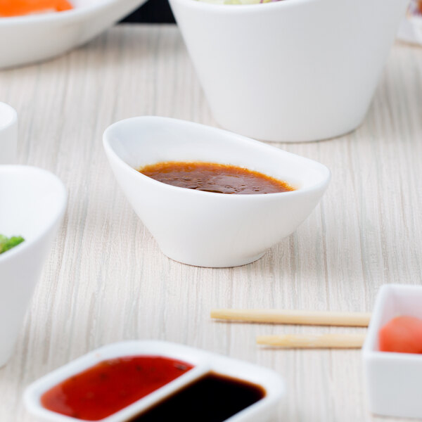 A white bowl with brown liquid in it on a table with bowls of food.