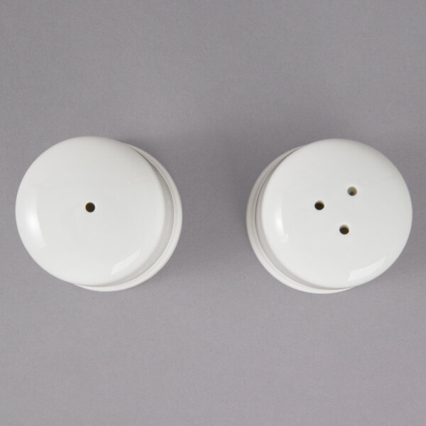Two white porcelain salt and pepper shakers with black dots on the top.