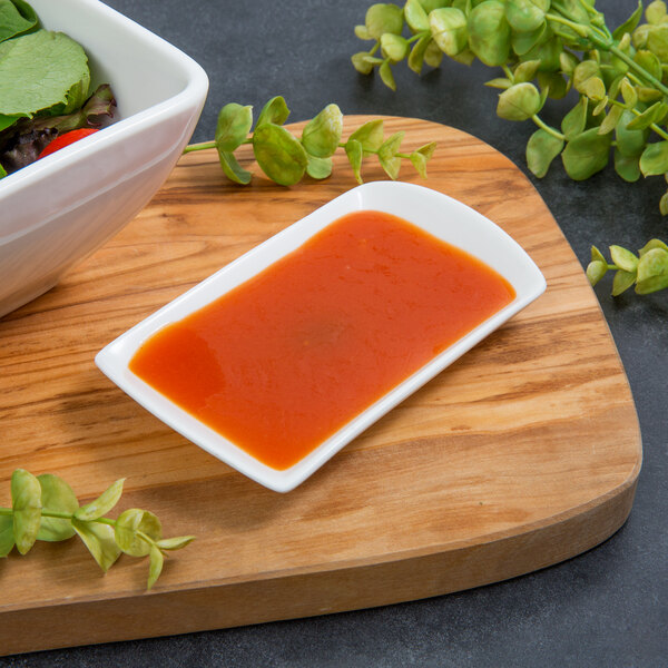 A white rectangular porcelain tid bit tray with bowls of salad and vegetables on a table.