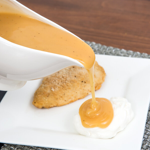 A white porcelain gravy boat pouring sauce into a white bowl.