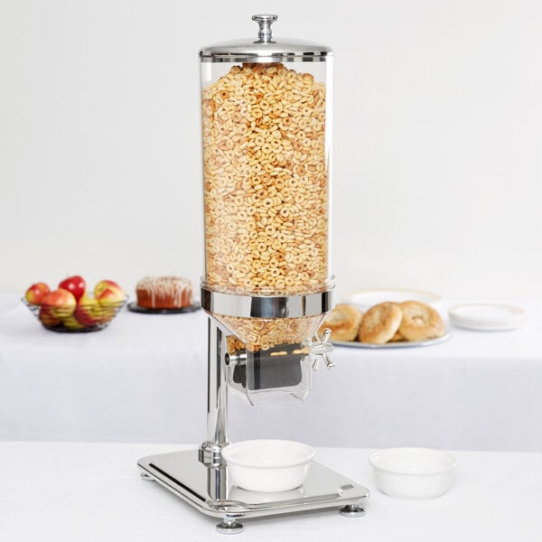 A Vollrath cereal dispenser filled with cereal next to a white bowl with a spoon.