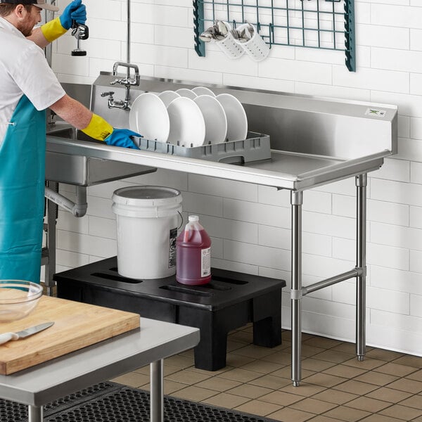 A man in blue gloves and an apron washing dishes on a Regency soiled dish table.