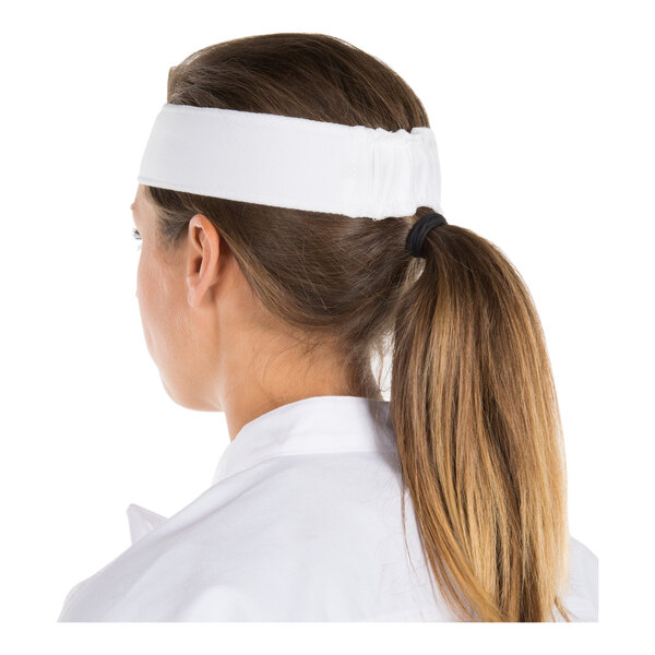 A person with long brown hair in a ponytail is wearing a wide white headband and a white collared garment, viewed from the back.