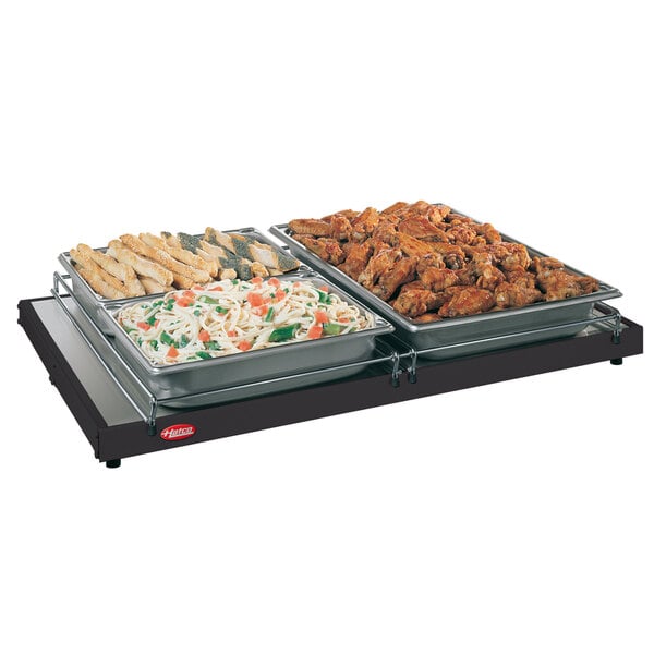 A Hatco Glo-Ray heated shelf with trays of pasta, vegetables, and chicken wings on a table.