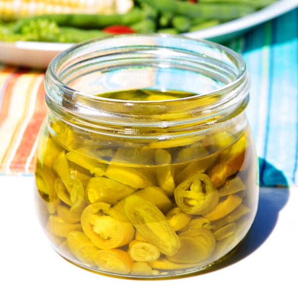 An American Metalcraft glass jar of jalapeno peppers on a table.