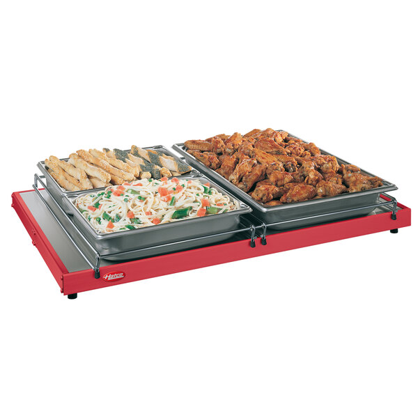 A red Hatco heated shelf with trays of food on a table.