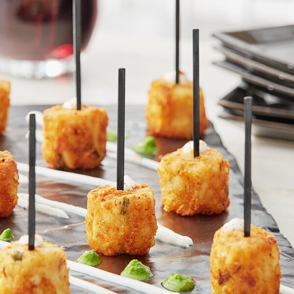 A plate of food with Royal Paper black plastic arrow picks on a table at a catering event.