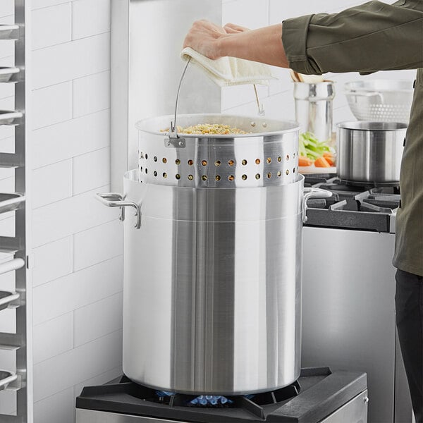 A man using a Winco aluminum steamer basket in a large pot to cook food.