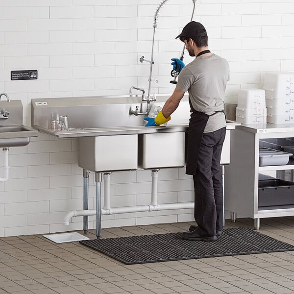 A man washing a Regency 3 compartment sink with drainboard.