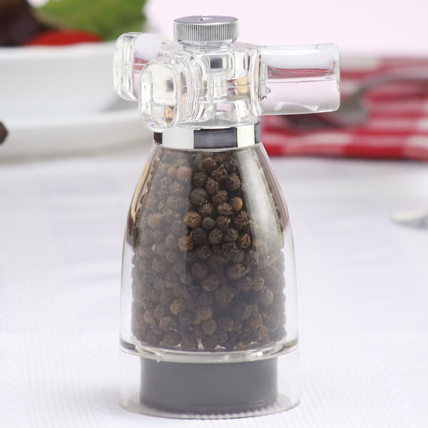 A Chef Specialties acrylic pepper mill with black peppercorns inside.