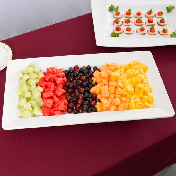 A Tablecraft white rectangular melamine tray with fruit and canapes on a table.