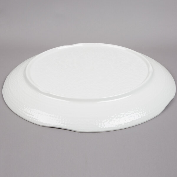 A Tablecraft white round melamine tray with a pebbled rim on a gray surface.