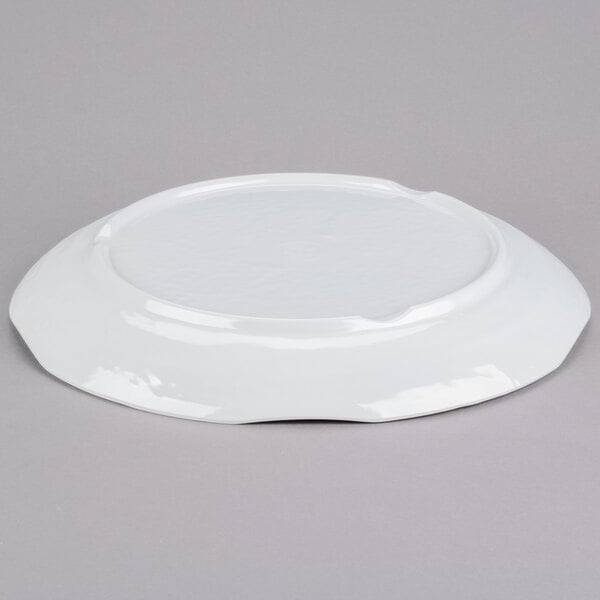 A Tablecraft white round melamine tray with a pebbled rim on a gray surface.