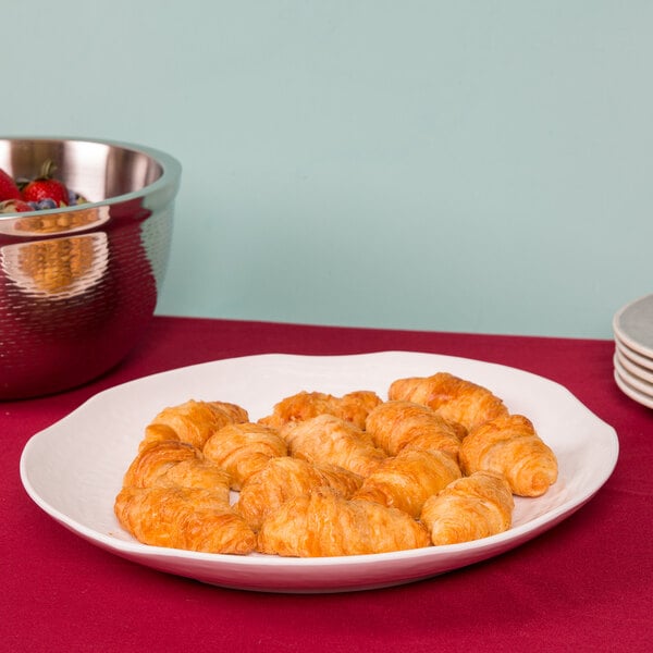 A Tablecraft white round pebbled melamine tray with croissants and fruit.
