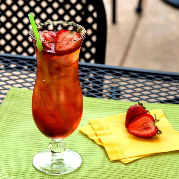 A Arcoroc hurricane glass of red liquid with strawberries on a green napkin.