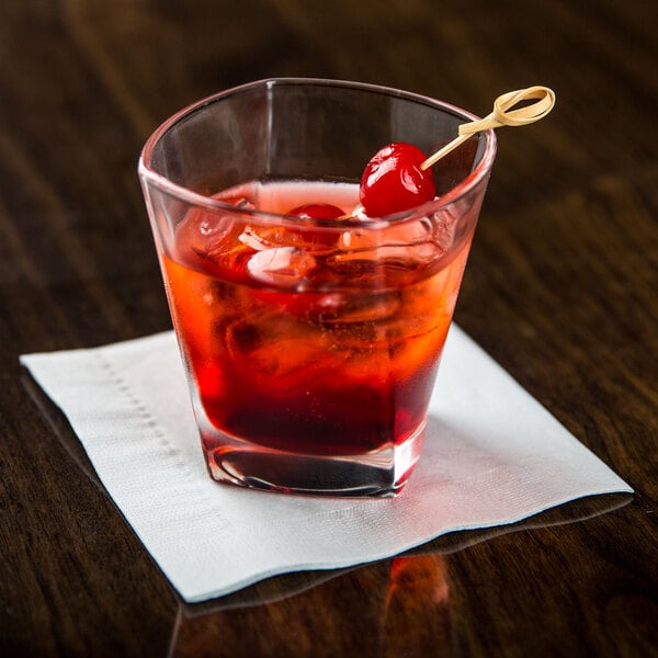 An Arcoroc Prysm rocks glass with a red drink and a cherry on top on a table.