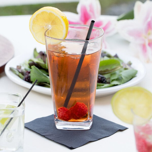 A glass of tea with a lemon slice and a straw on a table.