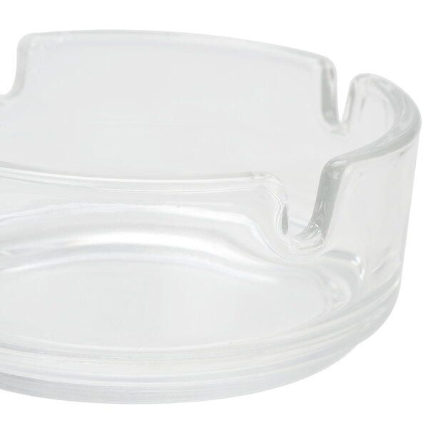 A close up of a clear glass Arcoroc ashtray with a small hole in the center.