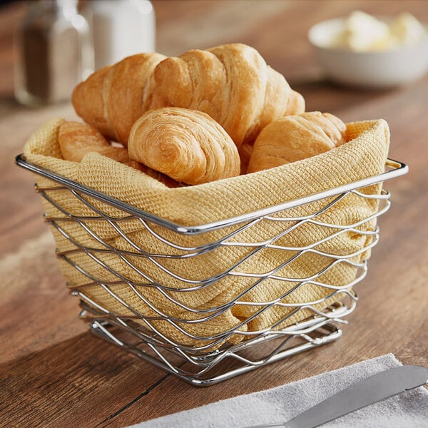 An American Metalcraft chrome square basket filled with croissants on a table.