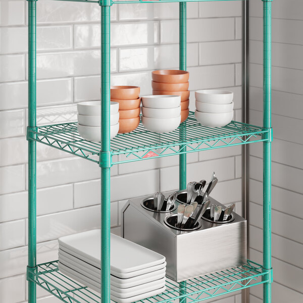 A green wire shelf unit with multiple tiers, holding bowls, plates, and utensils.