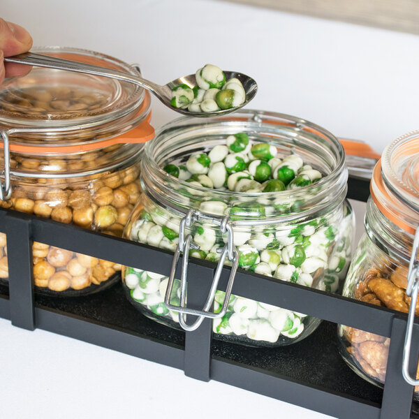 A person using a spoon to get nuts from a Cal-Mil rustic jar on a hotel buffet table.