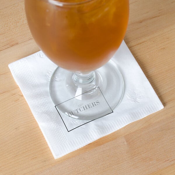 A glass of beer on a white Choice cocktail napkin on a table.