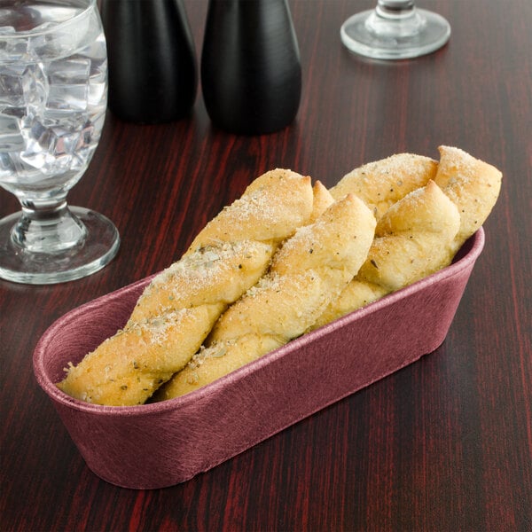 A black breadstick basket filled with bread sticks on a table with a glass of water.