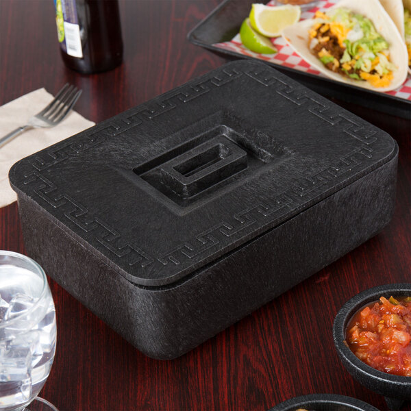 A black HS Inc. multi-purpose container with a square design and lid on a table with food and drinks.