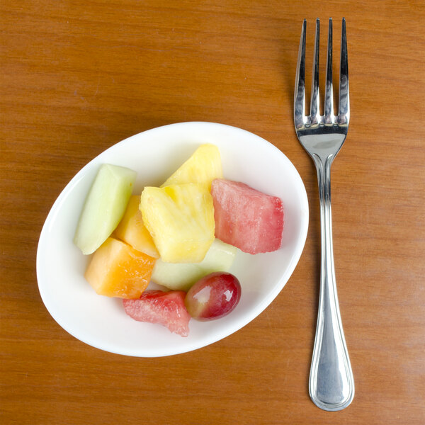 A Tuxton China bowl filled with fruit on a table with a fork.