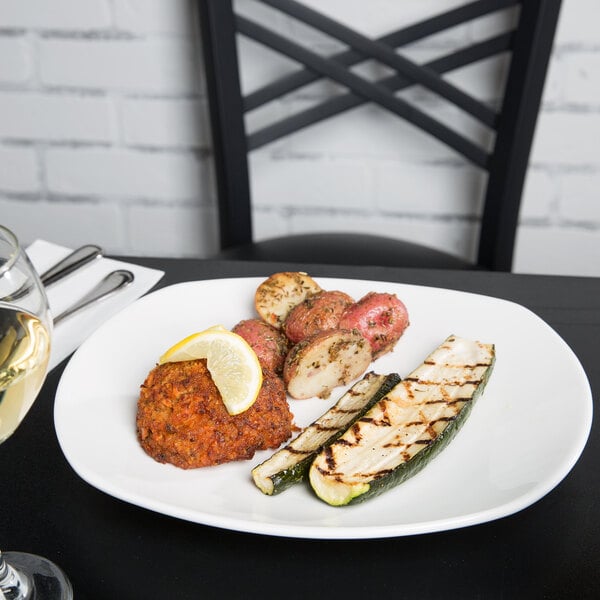 A white Tuxton china plate with food and a glass of wine on a table.