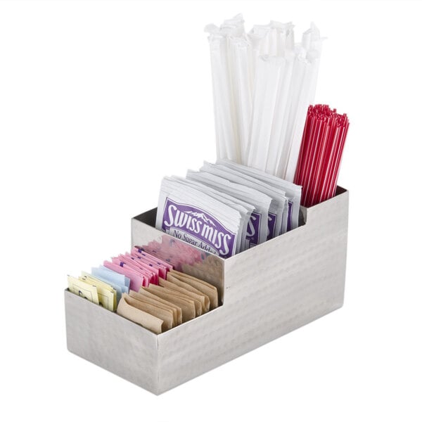 An American Metalcraft stainless steel bar caddy on a hotel counter filled with sugar packets and straws.