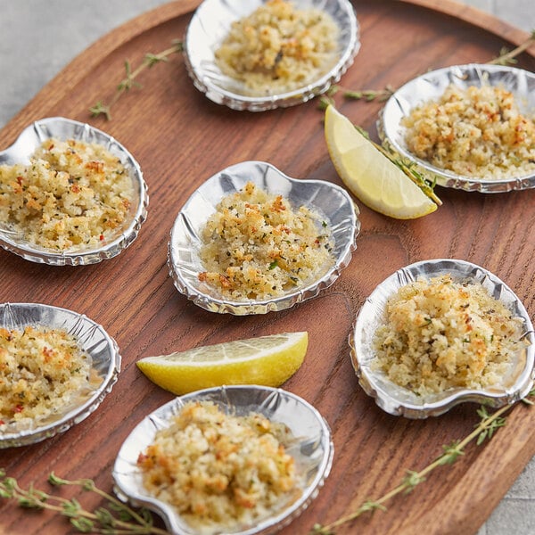 A wooden tray with six Royal Paper small foil clam shells filled with crab on a table.