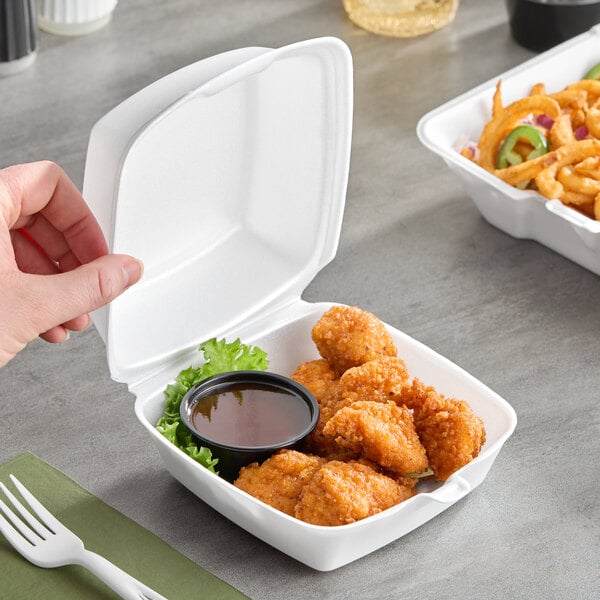 A white foam hinged lid container holding chicken nuggets, a dipping sauce, and a garnish.