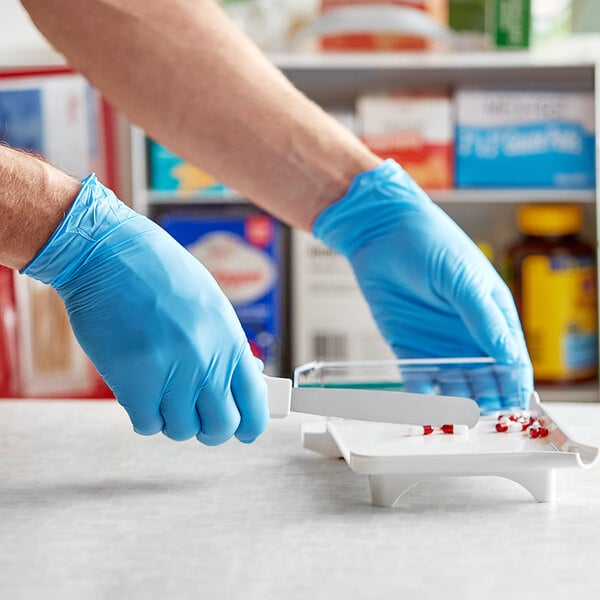 A person in blue Noble Products gloves using a knife on a white surface.